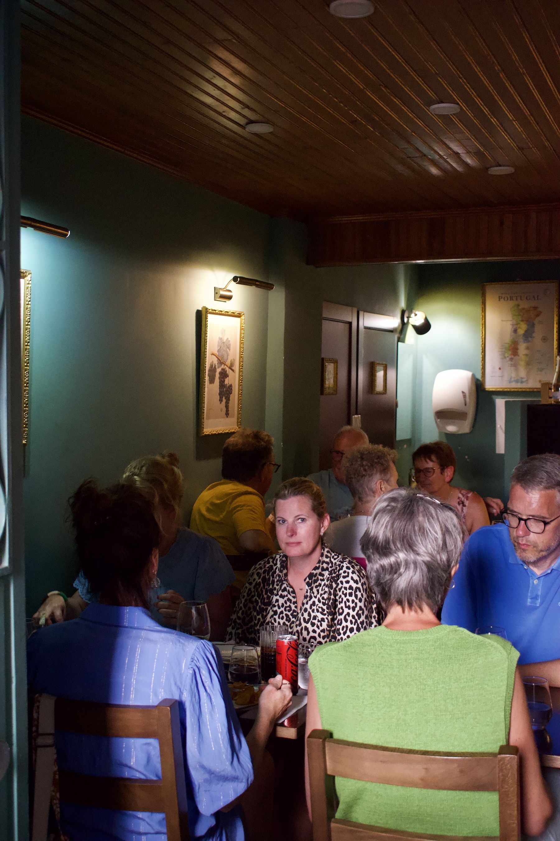 Sala cheia, com clientes à mesa e garrafeira ao fundo