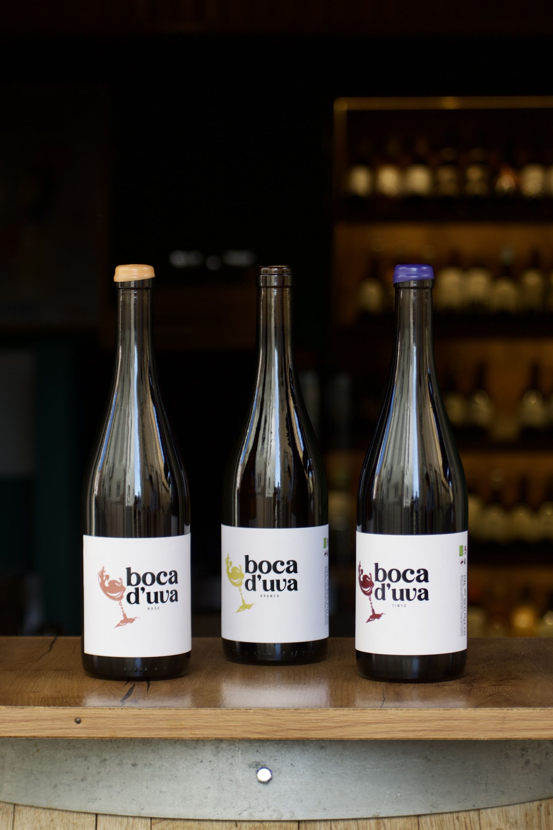 Três garrafas Boca d'Uva — rosé, branco e tinto — sobre o balcão